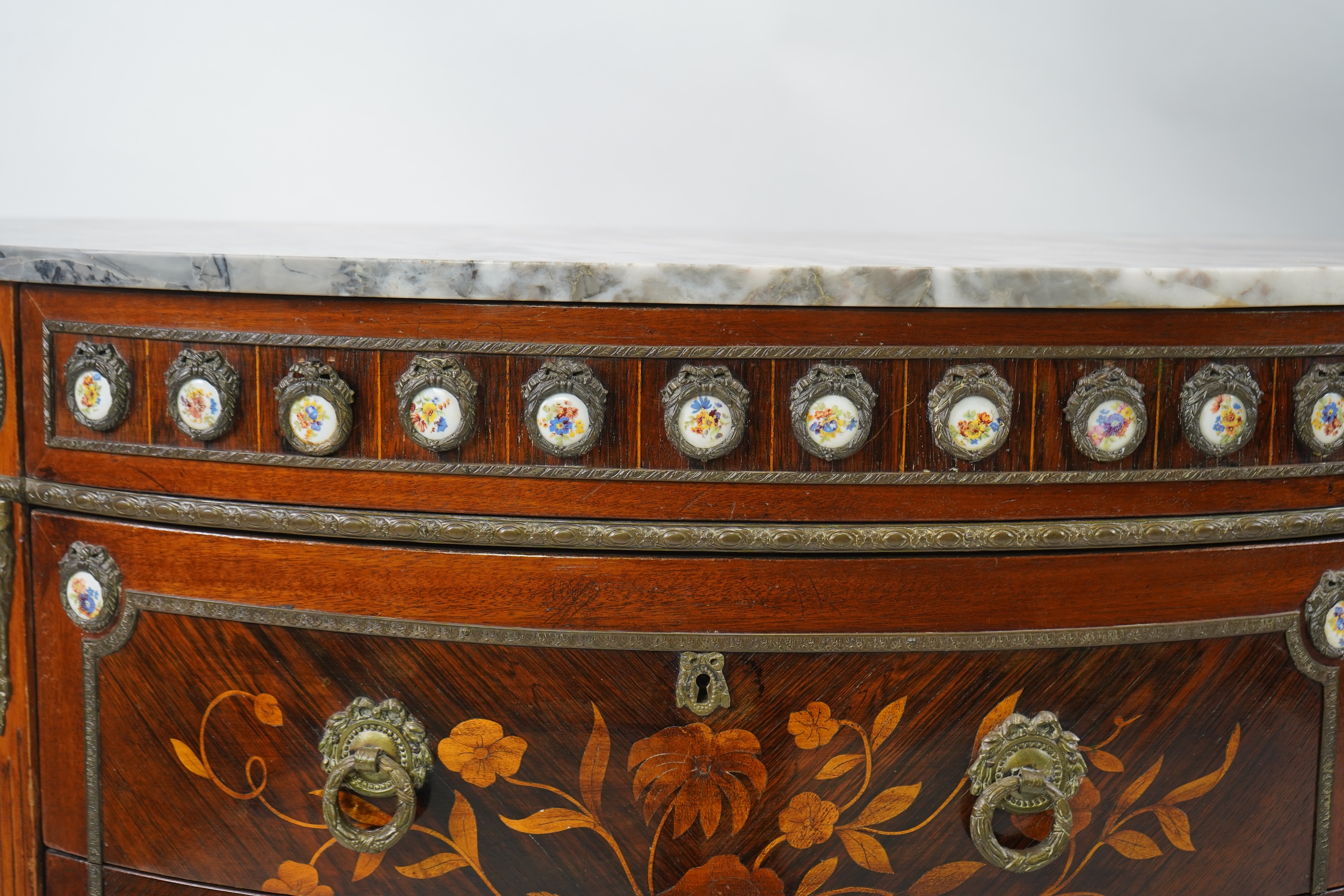 A pair of early 20th century French marquetry inlaid, gilt metal and porcelain mounted rosewood and beech demi-lune commodes